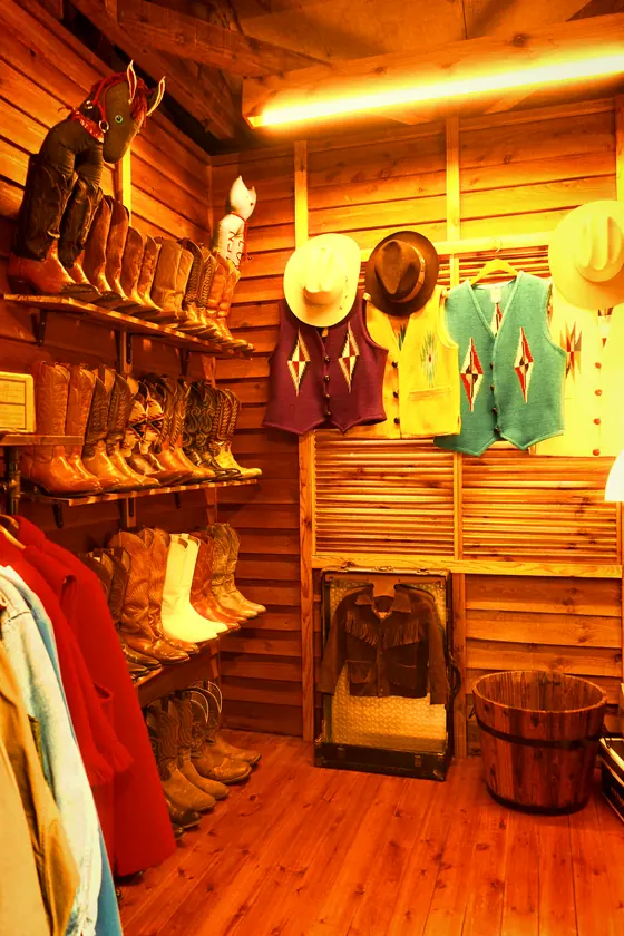 A western-wear shop lit by one warm tube, shot with amber sun '74
