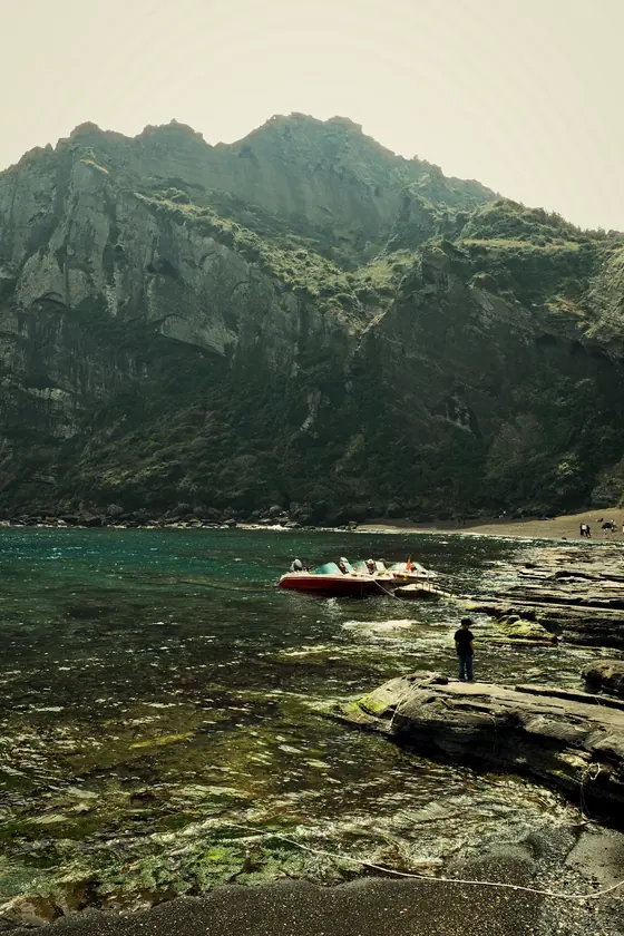 A green sea cliff and a boat on clear water, shot with costa verde