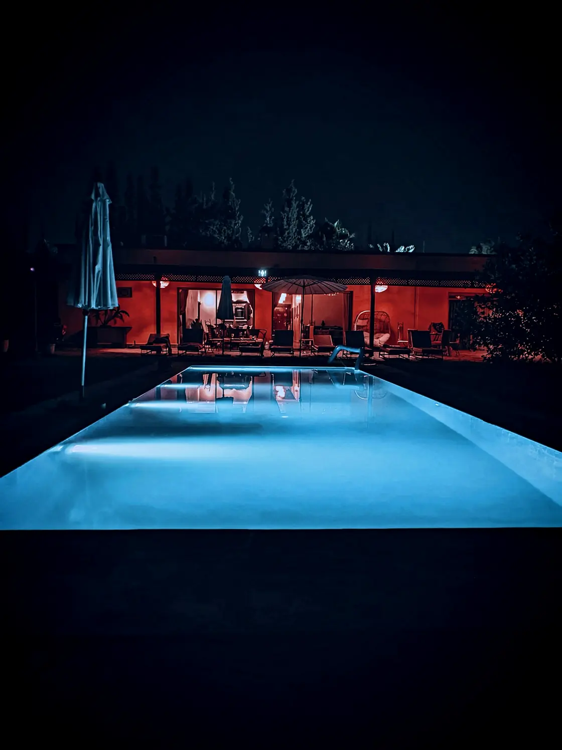 A lit swimming pool outside a house at night, shot with cyberpunk neon night